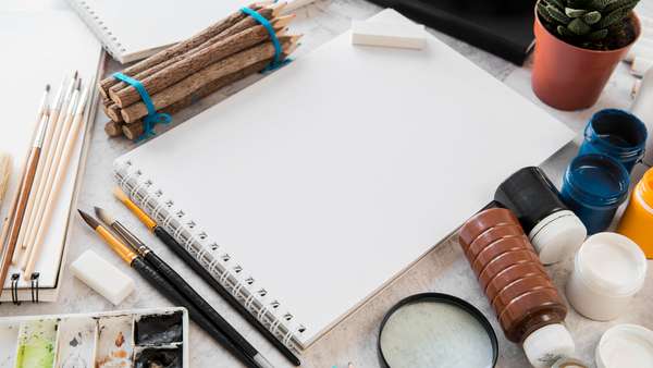 Materiais de desenho e caderno sobre uma mesa clara